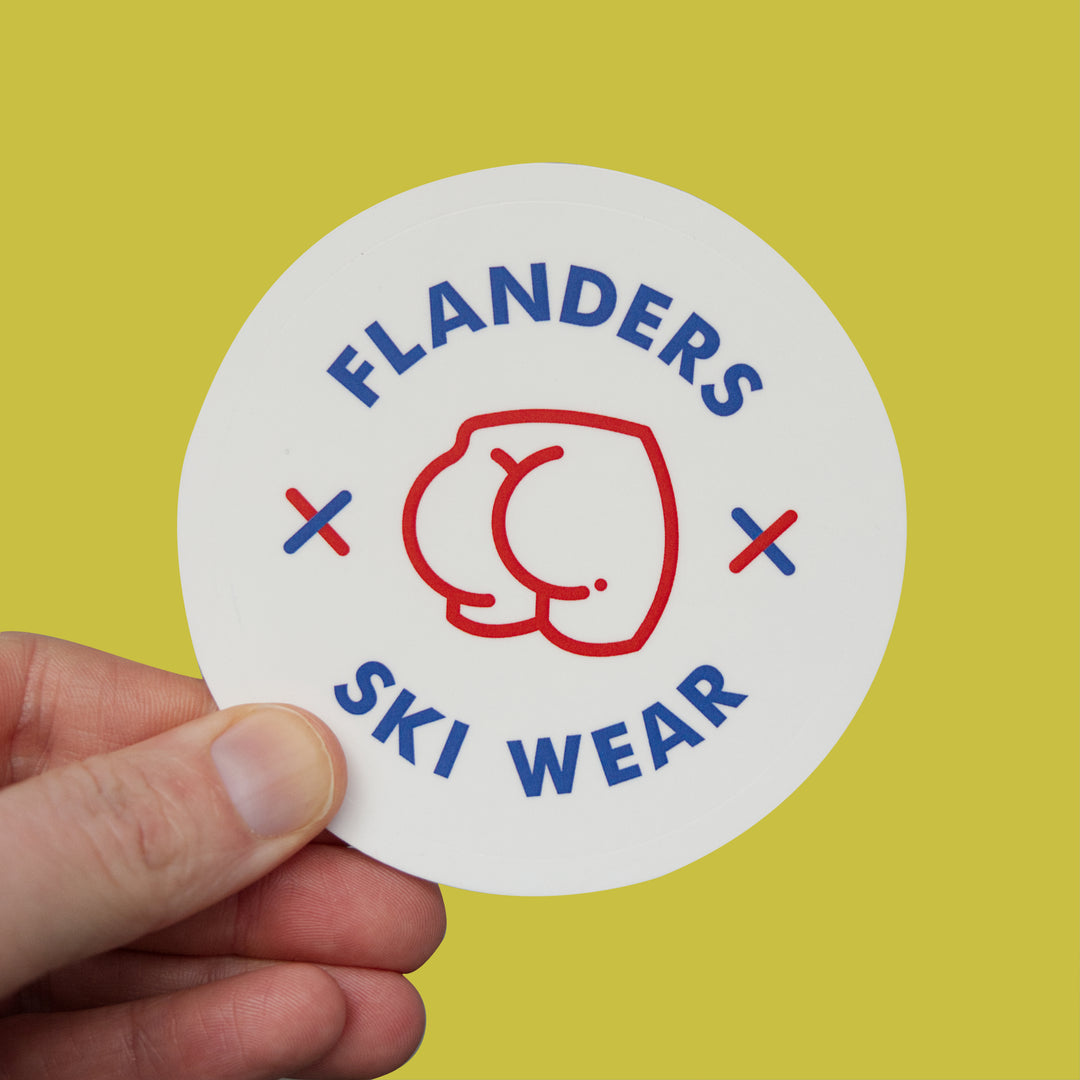Sticker with 'Flanders Ski Wear' logo held by a hand against a yellow background