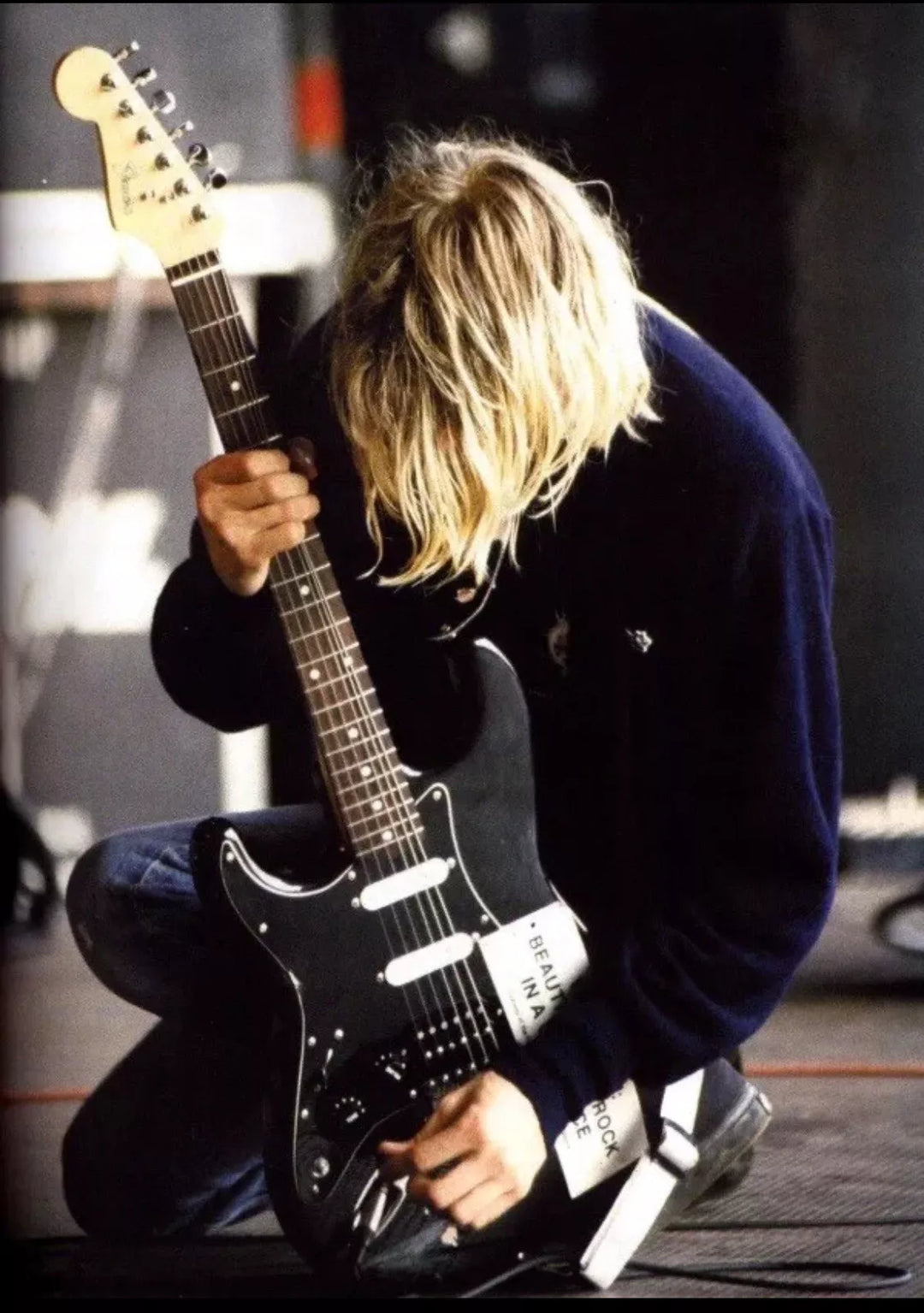Person playing a black electric guitar on stage with a blurred background