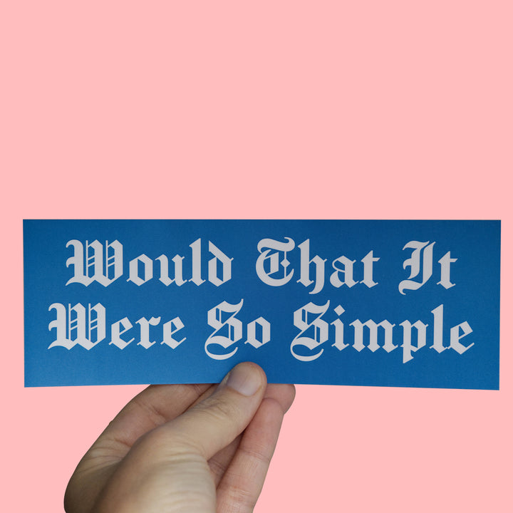 A hand holding a blue rectangular sticker with white gothic text that reads &